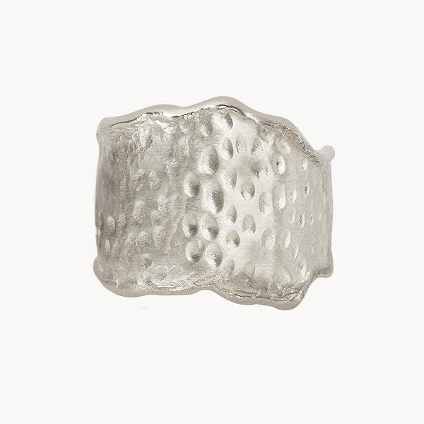 The sweetness of honey ring silver by bluboho is a wide, textured sterling silver ring with an irregular design. The surface boasts a hammered finish with raised and indented patterns, and the uneven edges lend it a rustic and organic appearance. The background is plain white.