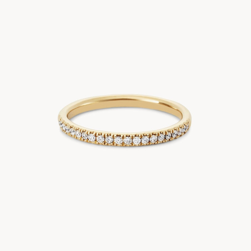 The Endalaus II ring by beloved by bluboho, crafted from 14k yellow gold and adorned with a continuous row of small white diamonds on the upper half, showcases a simple yet elegant design. It is set against a plain white background, highlighting its intricate details and shimmering effect.