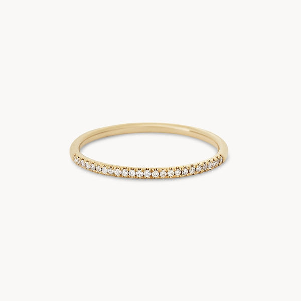 The Endalaus I ring by beloved by bluboho is a delicate piece crafted from 14k yellow gold featuring a thin, circular band. The top half of the band is adorned with small, sparkling white diamonds, resulting in an elegant and minimalist design. The background is plain white.