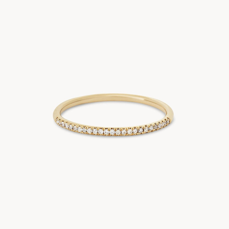 The Endalaus I ring by beloved by bluboho is a delicate piece crafted from 14k yellow gold featuring a thin, circular band. The top half of the band is adorned with small, sparkling white diamonds, resulting in an elegant and minimalist design. The background is plain white.