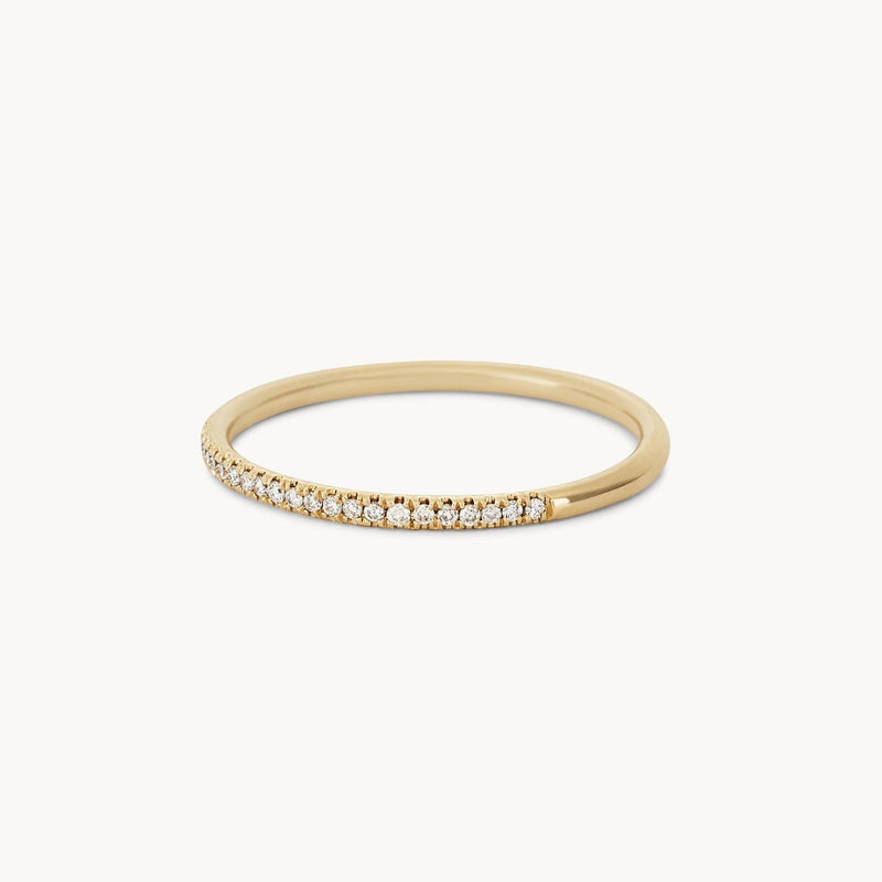 The Endalaus I ring by beloved by bluboho in 14k yellow gold features a row of small, shimmering white diamonds that span half its circumference, creating an elegant and minimalist design against a plain white background.