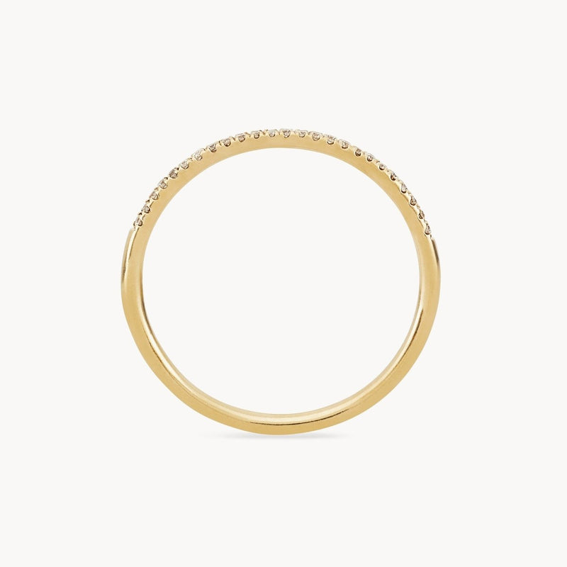 The Endalaus I ring by beloved by bluboho is a delicate gold band crafted from 14k yellow gold, featuring small, evenly spaced white diamonds set along the upper half of the band. The ring boasts a simple, elegant design with a smooth, polished finish and is showcased against a plain white background.