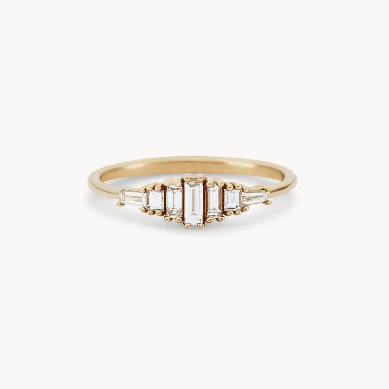 The "Daybreak band" by beloved by bluboho features a central elongated rectangular white diamond, flanked by two smaller rectangular diamonds on each side, all set in a sleek, minimalist 14k yellow gold band. The diamonds are arranged in a symmetrical, stepped pattern.