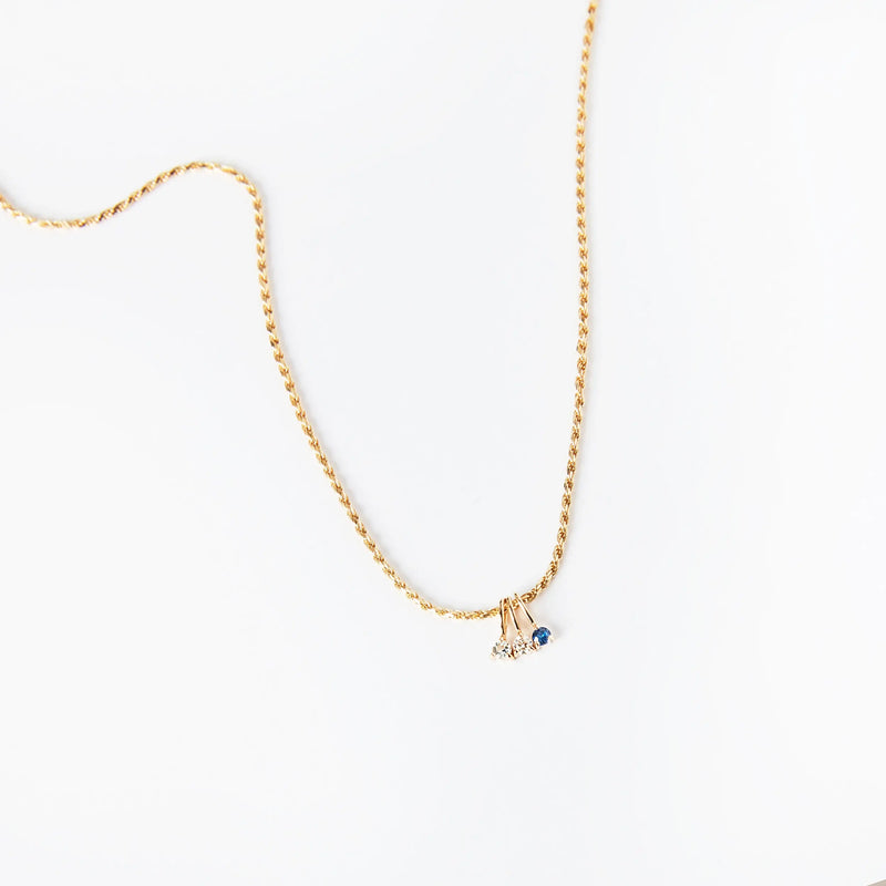 A delicate gold chain necklace by bluboho featuring the Serendipity May Birthstone Charm, crafted in 10k yellow gold with two exquisite pendants: a clear, teardrop-shaped stone that may be a diamond and a small, round emerald. The plain white background accentuates the simplicity and elegance of this beautiful piece.