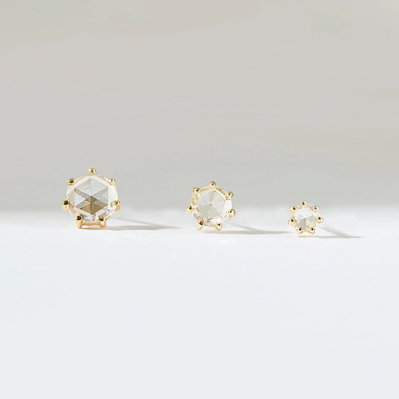 Three "Nova Earring - 14k Yellow Gold, White Diamond" by Bluboho of varying sizes set in gold. The largest stud is on the left, the medium one in the middle, and the smallest on the right. They are arranged in a row against a light-colored background.