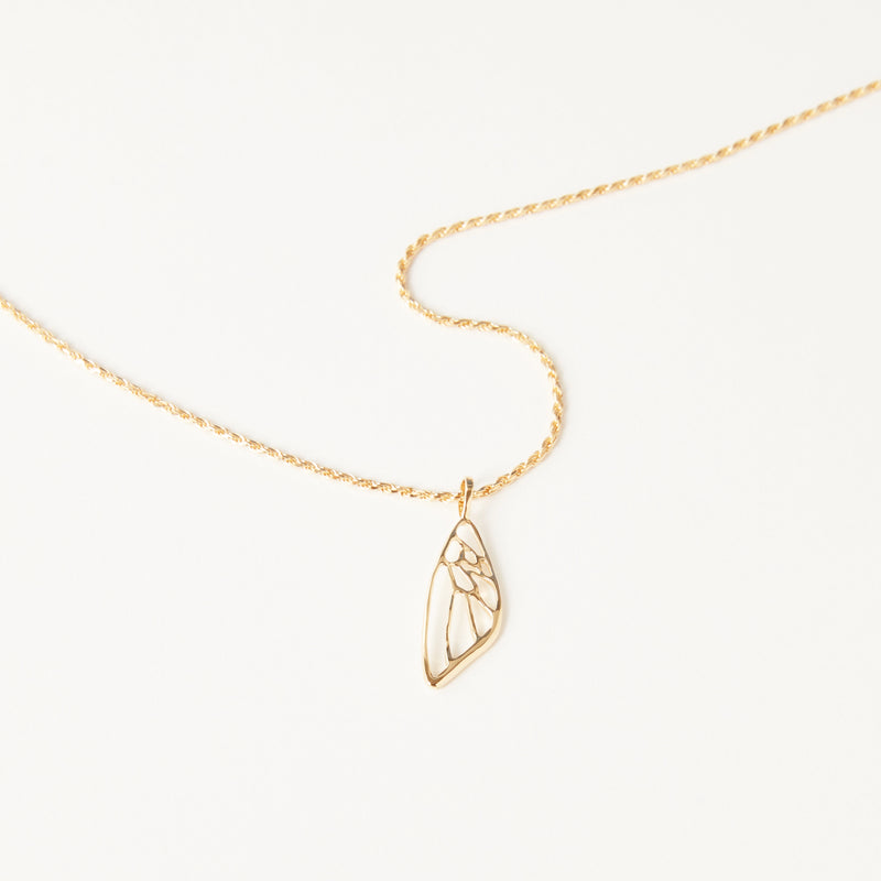 A delicate bluboho necklace in 10k yellow gold features a charming pendant shaped like an elongated, openwork butterfly wing. The pendant's minimalist and symmetrical design adds a touch of elegance to the accessory, which rests beautifully on a white background.