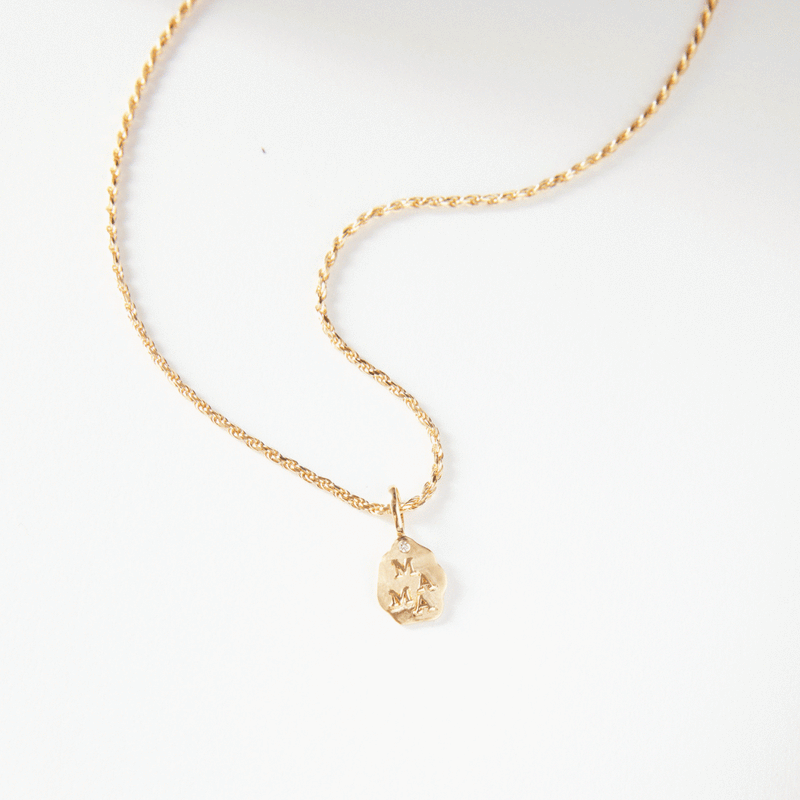 A gold necklace from bluboho, named "the mama charm - 10k yellow gold," showcasing a twisted chain and an irregularly shaped pendant. The pendant is engraved with the letters "M" and "A" and is displayed on a white background.