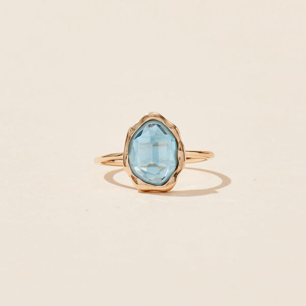 The london blue topaz mood ring by bluboho features an oval-shaped blue topaz gemstone set in a simple, elegant 14k yellow gold band. The gemstone catches the light, giving it a slight shimmer. The ring is presented against a plain, light beige background.