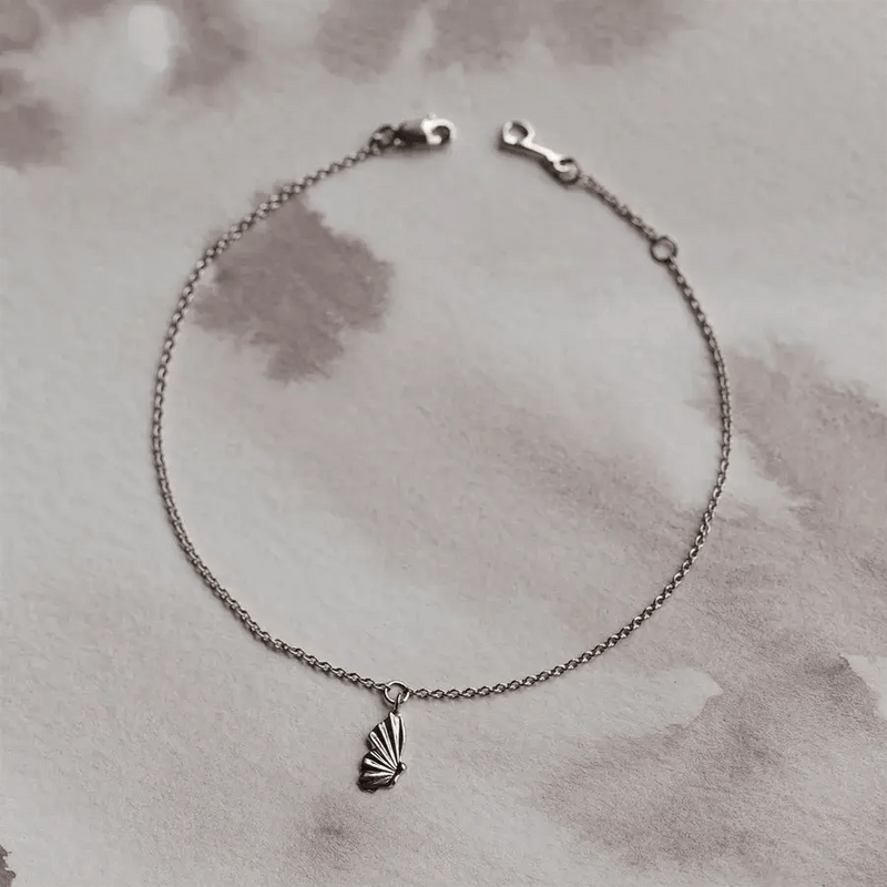 Here is the revised sentence using the given product data:

A delicate sterling silver chain bracelet featuring a small butterfly wing charm positioned at the center. The metamorphosis butterfly wing bracelet by bluboho is arranged in a circular shape on a soft, monochromatic background with varying shades of gray. The clasp is visible at the top of the bracelet.