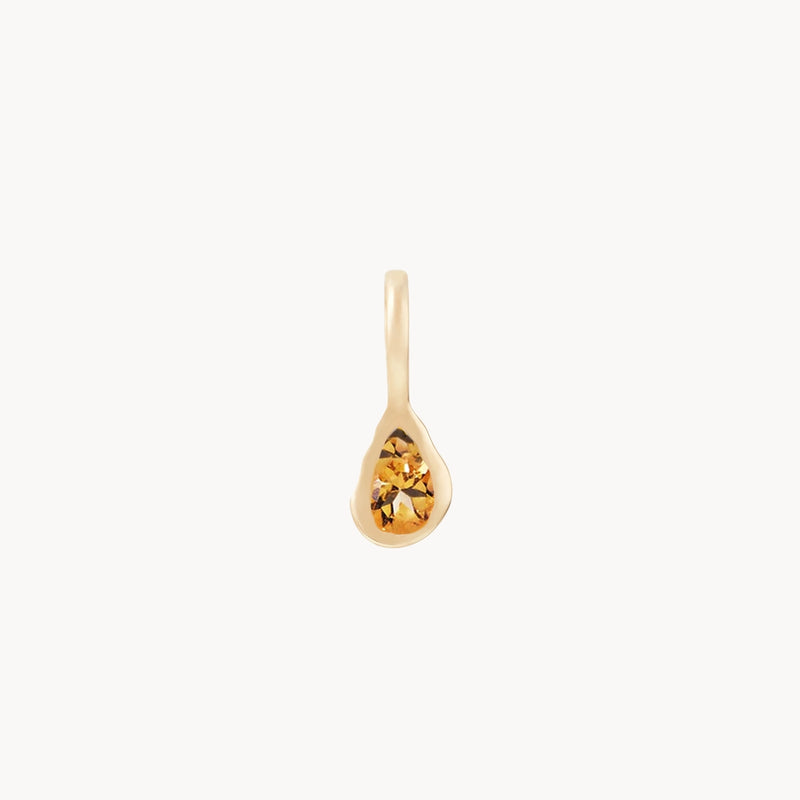 A small, 10k yellow gold charm named "pear citrine november mood birthstone charm" by bluboho, featuring a faceted, amber-colored citrine gemstone in the center. The pendant boasts a sleek and minimalist teardrop design with a loop at the top for easy attachment to a necklace or bracelet. Displayed against a plain white background.