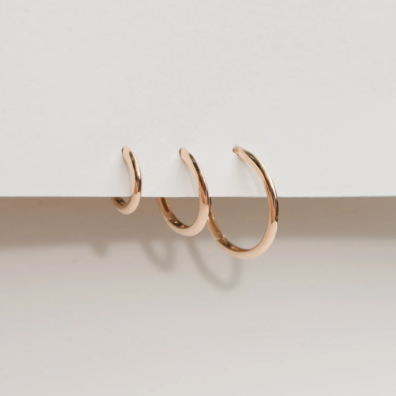 Three hoop earrings, named the dagger large hoop - 14k yellow gold hoop by bluboho, are displayed against a plain white background. The earrings decrease in size from right to left, showcasing a polished, shiny surface and a simple, elegant design.