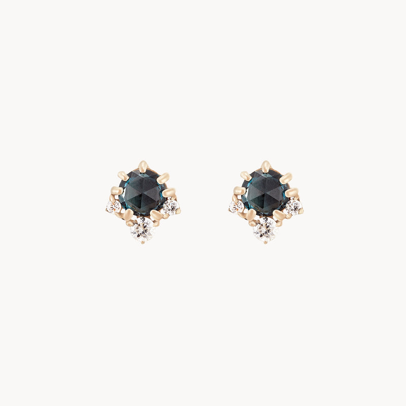 A pair of sophisticated stud earrings, the Full Moon Glow Diamond London Blue Topaz Earrings by bluboho, feature round blue topaz gemstones encircled by sparkling diamonds. These elegant earrings are set in 14k yellow gold.
