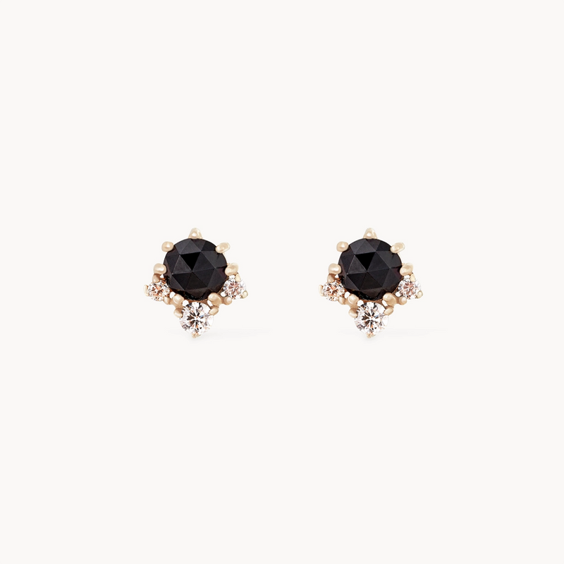 The "Full Moon Glow Diamond Black Onyx Earring" by Bluboho features faceted black onyx stones set in a refined 14k yellow gold setting. Each earring is adorned with three small diamonds around the main black onyx, adding a touch of sparkle and sophistication against a plain white background.