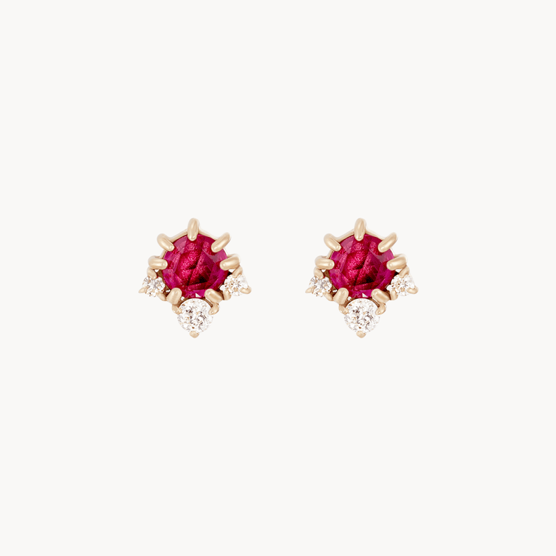 The full moon glow diamond ruby earrings by bluboho feature a central, vibrant ruby encased in 14k yellow gold, with small, sparkling diamonds arranged around the ruby center, creating a stylish and luxurious design.