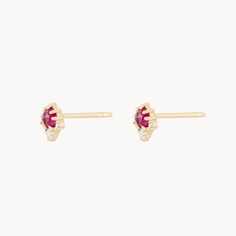 The Full Moon Glow Diamond Ruby Earrings by bluboho are crafted from 14k yellow gold, featuring a central ruby gemstone and accented with a small diamond. These elegant stud earrings are designed for pierced ears and are set in a prong setting. They are displayed against a white background.