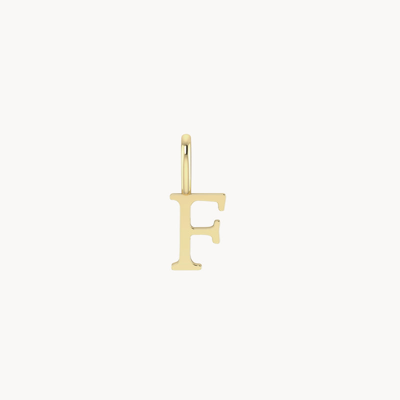 A simple gold pendant in the shape of the letter "F" is shown. The bluboho letter charm - 10k yellow gold has a small loop at the top for attaching to a chain or bracelet. The design is plain and elegant, with a smooth, polished finish.
