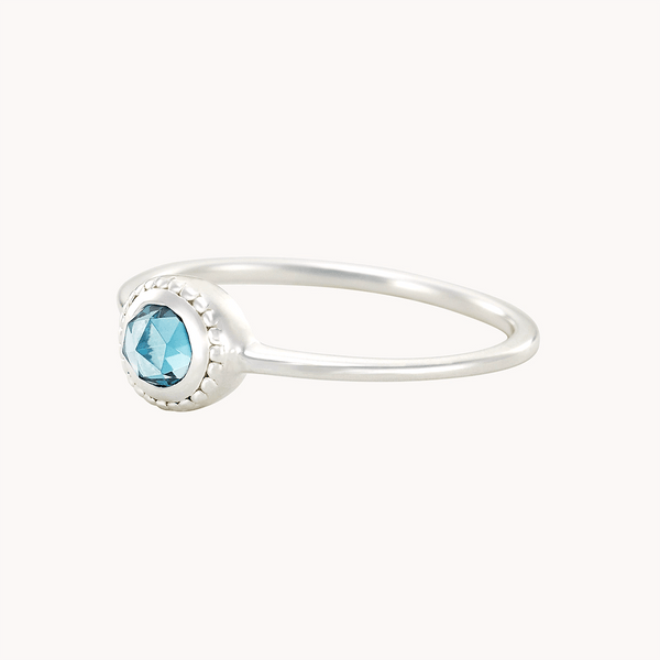 The bluboho full moon London blue topaz ring, crafted from sterling silver, features a single round faceted blue gemstone in a bezel setting. The thin, smooth band complements the brilliant gemstone which catches the light beautifully. Displayed on a plain white background, this delicate silver ring exudes elegance.