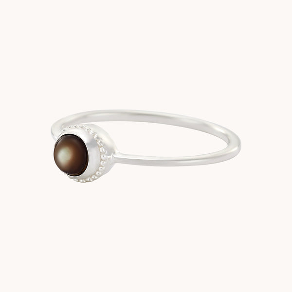 The full moon dark mother of pearl ring in silver by bluboho showcases a delicate design with a dark brown round stone set in a polished bezel and accented with a beaded texture around the stone, all presented against a plain white background.