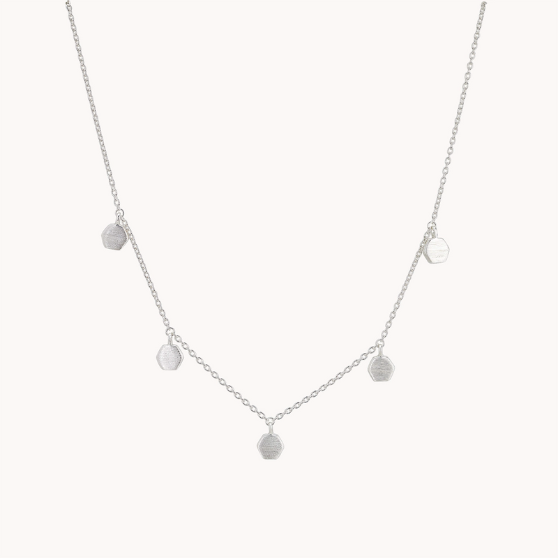 The honeysuckle necklace silver by bluboho showcases a delicate sterling silver chain adorned with five evenly spaced small hexagon-shaped charms. The minimalist design of this necklace imparts a modern and elegant aesthetic against its plain white background.