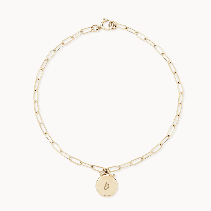 A delicate gold chain bracelet featuring elongated, rectangular links. It has a circular charm with the letter "b" engraved on it, attached via a small loop. The bluboho Imprint Forest Bracelet - 14k Gold, Engravable is laid out in a circular shape on a plain white background.