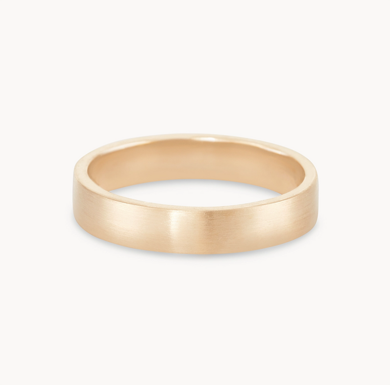 The Infinity Love Band Brushed by Beloved by Bluboho is a 14k yellow gold ring with a sleek, flat, unadorned design and a brushed finish. It features a smooth, rounded inner surface and a flat top surface, embodying a modern and minimalistic aesthetic.