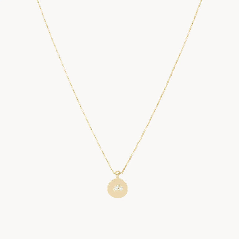 The kindred spirits lean on me medallion necklace by bluboho is a delicate 14k yellow gold piece with a fine chain that features a small, round pendant. The pendant, engraved with a tiny bee design and adorned with diamonds, adds a subtle and elegant touch. The combination of the chain and the bee pendant radiates simplicity and charm.