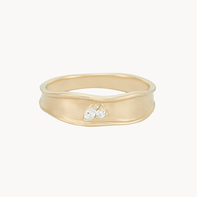 The "kindred spirits lean on me band ring" by bluboho is crafted in 14k yellow gold and showcases an organic, wavy design on its smooth matte-finish band, accented by a cluster of three small diamonds that add a touch of sparkle.