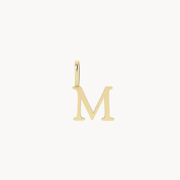 A small bluboho letter charm - 10k yellow gold in the shape of the letter "M" with a jump ring at the top for attaching to a necklace or bracelet. The surface of the charm is smooth and shiny.