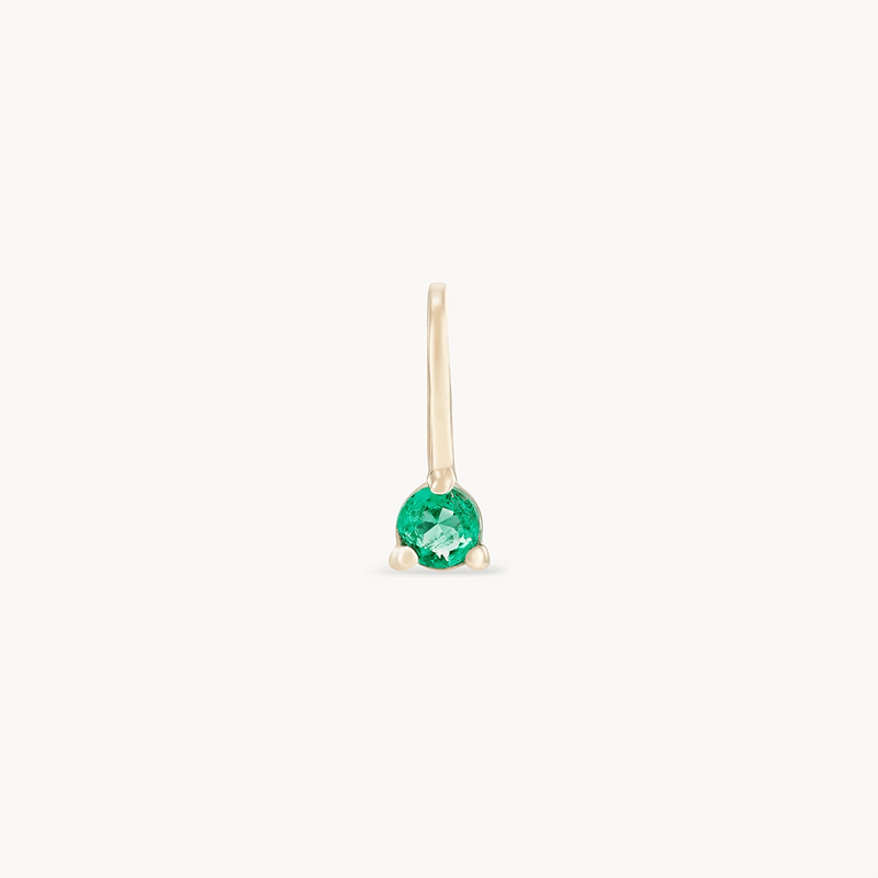 The serendipity may birthstone charm by bluboho is an elegant 10k yellow gold earring, featuring a single round emerald gemstone secured by three delicate gold prongs. Its minimalist and refined design includes a sleek and slender gold hook for attaching to the ear.