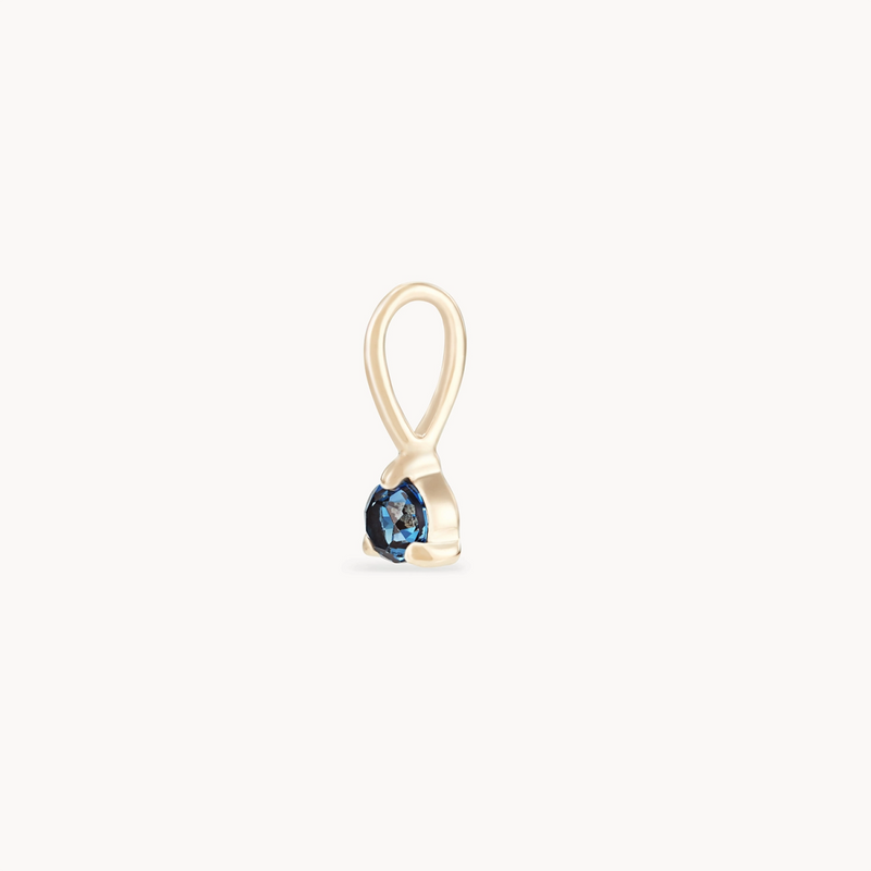 Introducing the serendipity september birthstone charm by bluboho, crafted from 10k yellow gold. This minimalist charm features a ribbon-shaped design with a loop at the top and a small, round sapphire set at the bottom. The polished finish of the gold complements the deep blue gemstone, adding an elegant touch to this exquisite accessory. Displayed on a white background for clarity.