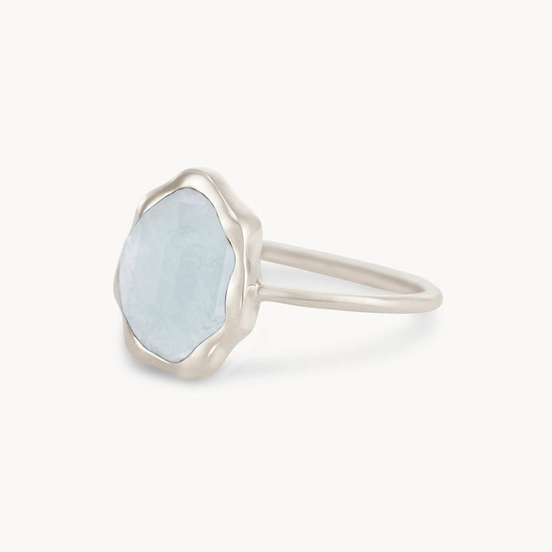 A blue chalcedony mood ring from bluboho, featuring a light blue, faceted gemstone set in a slightly wavy bezel setting. The sterling silver band is simple and elegant, showcased against a plain white background.