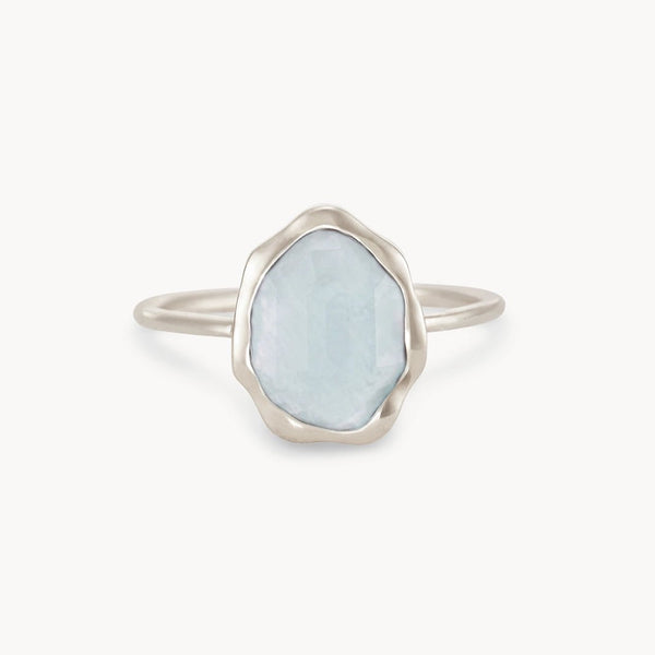 The bluboho blue chalcedony mood ring in sterling silver showcases a delicate wavy, irregular border that beautifully frames an oval-shaped, translucent pale blue gemstone. The simple and metallic band enhances the ethereal quality of the central stone, resulting in a minimalistic and elegant design.