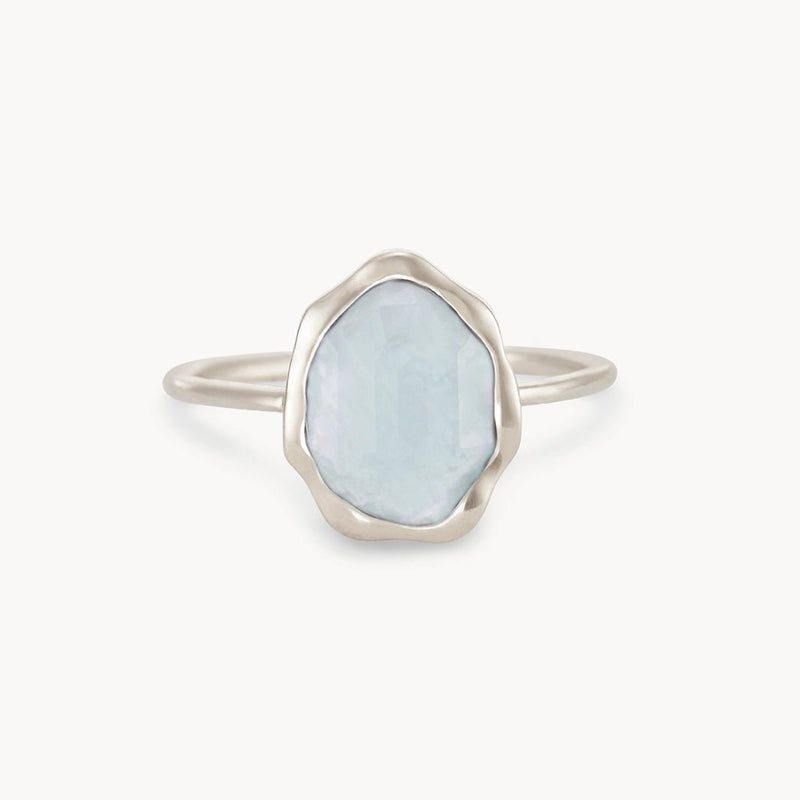 The bluboho blue chalcedony mood ring in sterling silver showcases a delicate wavy, irregular border that beautifully frames an oval-shaped, translucent pale blue gemstone. The simple and metallic band enhances the ethereal quality of the central stone, resulting in a minimalistic and elegant design.