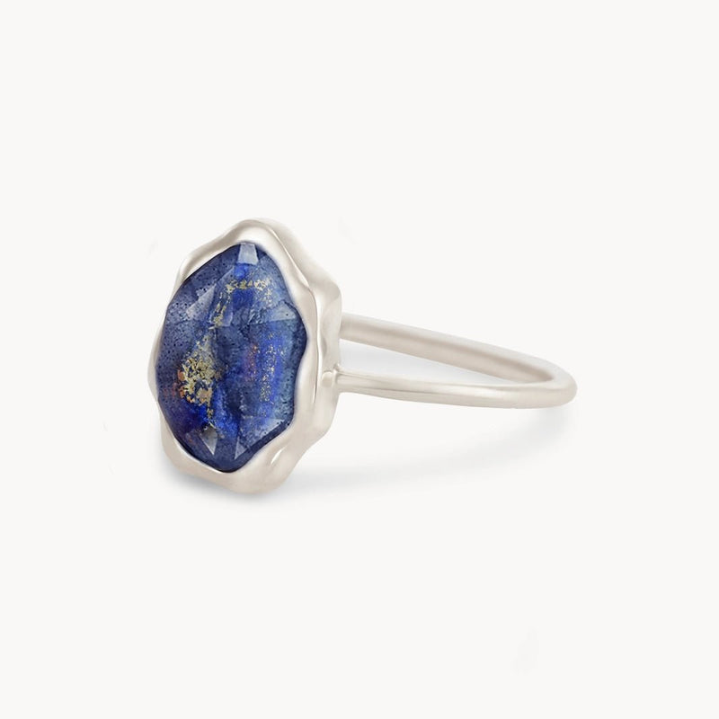 A close-up view of the bluboho lapis lazuli mood ring in sterling silver, showcasing a large, uniquely-shaped blue lapis lazuli stone with hints of gold. The thin and smooth ring band draws attention to the distinctively cut and textured gemstone. The background is a clean, white surface.