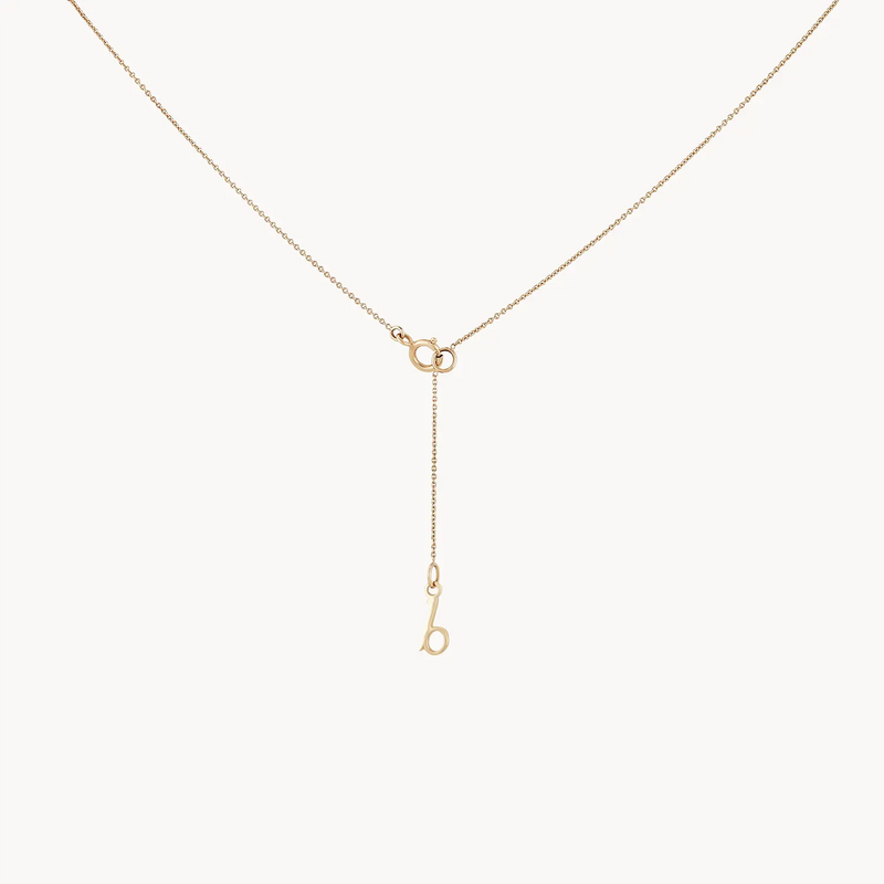 A delicate wildflower tanzanite petal necklace - 14k yellow gold, tanzanite by bluboho with a minimalist design featuring a small lowercase letter 'b' charm attached to a thin, extended chain hanging from a central clasp. The necklace has a fine, elegant chain and a sleek, modern look.