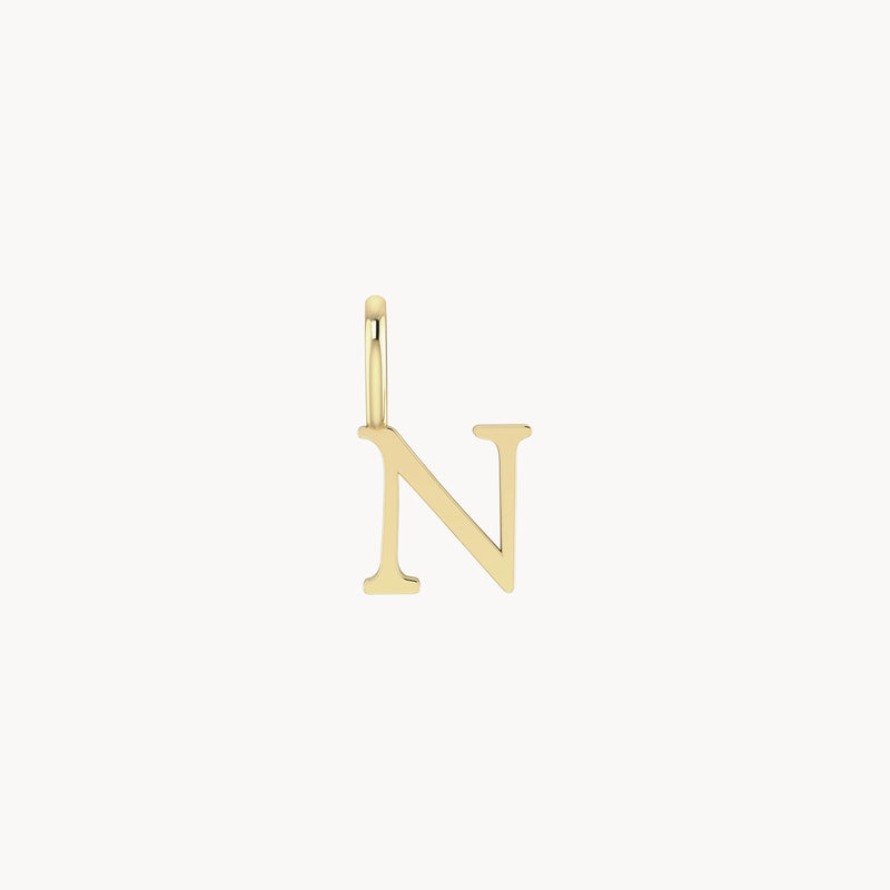 A bluboho letter charm - 10k yellow gold is displayed against a white background. The charm has a smooth finish and is attached to a small circular loop at the top.