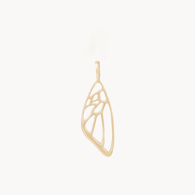 The "butterfly wing charm - 10k yellow gold" by bluboho is an exquisite gold pendant designed to resemble a butterfly wing. It features openwork details that mimic the intricate veining of a wing, lending it an airy and elegant appearance. A simple, small loop at the top allows it to hang gracefully. The background is white.