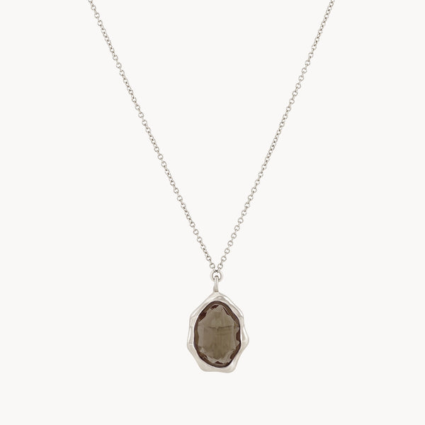 The smoky quartz mood necklace from bluboho features a central pendant with an irregularly shaped, faceted smoky quartz gemstone surrounded by a sterling silver bezel setting. The fine and evenly linked chain enhances the simple yet elegant design of this jewelry piece.