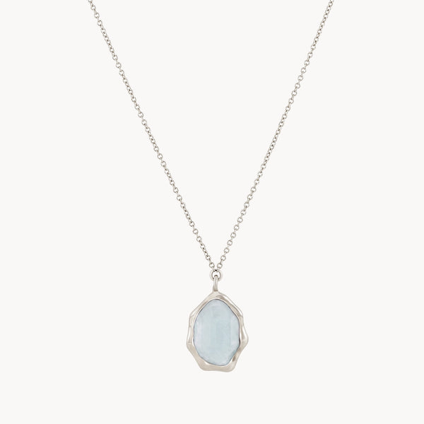 The blue chalcedony mood necklace from bluboho features a delicate sterling silver chain with a light blue, irregularly shaped blue chalcedony stone set in a smooth silver frame as the pendant. The organic, natural appearance of the pendant hangs gracefully at the center of the necklace.