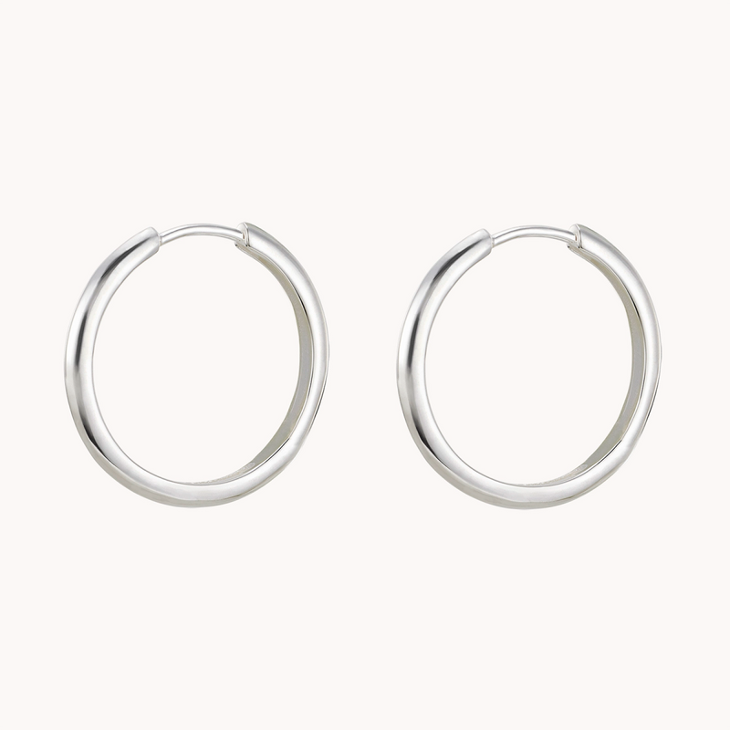 A pair of sleek, minimalist hoop earrings called the "dagger large hoop silver" from bluboho. These polished silver earrings showcase a smooth and shiny surface, featuring a small gap at the top where the hoop closes. They are elegantly displayed on a plain white background.