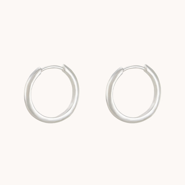 A pair of bluboho's dagger medium hoop silver earrings elegantly displayed against a neutral background, each forming a nearly perfect circle with their smooth, polished surface. These thin yet sturdy earrings exude a minimalist design.