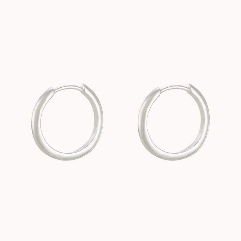 A pair of bluboho's dagger medium hoop silver earrings elegantly displayed against a neutral background, each forming a nearly perfect circle with their smooth, polished surface. These thin yet sturdy earrings exude a minimalist design.