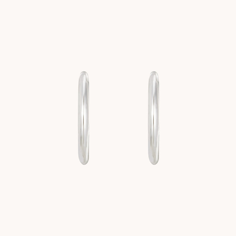 Two "dagger medium hoop silver" earrings by bluboho are displayed against a plain, off-white background. The earrings are simple, smooth, and thin, emphasizing their sleek design and subtle shine.