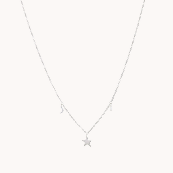 The Bright Star White Topaz Baguette Necklace in sterling silver, by bluboho, features a delicate chain adorned with three small charms: a crescent moon, a star centerpiece embellished with white topaz, and an asymmetrically positioned rectangular bar.