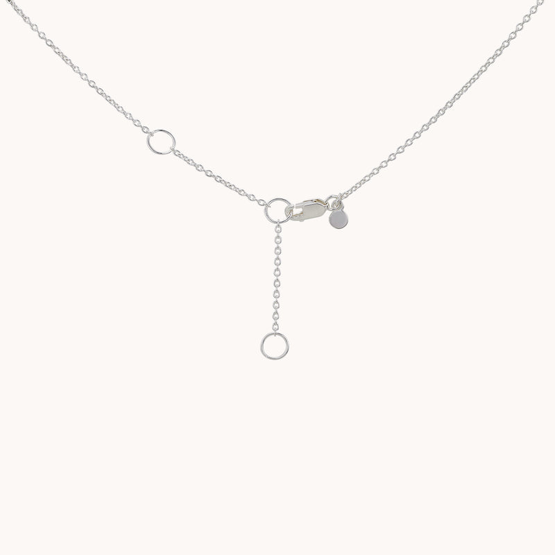 A delicate crescent moon necklace from bluboho, made of sterling silver, showcased on a plain background. The necklace features a thin chain with small circular links and a small crescent moon charm. One end has a small round charm, while the other end has a clasp and an extender with a circular ring at the end.