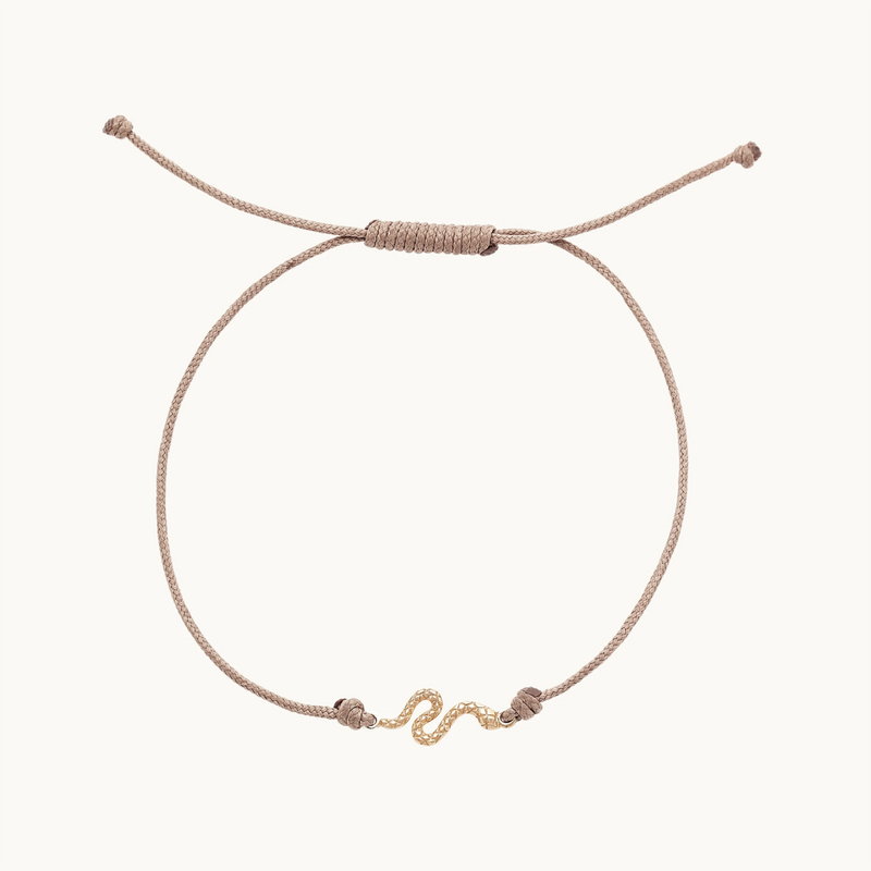 The serpent contemplation cord bracelet by bluboho features a thin taupe cord with an adjustable sliding knot mechanism and a delicate 10k yellow gold S-shaped accent at the center. The bracelet is displayed against a plain white background.