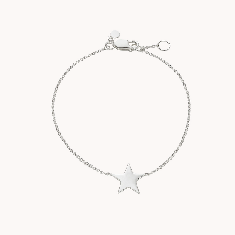 The stella star bracelet silver by bluboho is a delicate piece featuring a fine chain and a small, shiny star charm at its center. Crafted from sterling silver, it boasts a lobster clasp for fastening and an adjustable chain with an extra ring for size customization. The background is plain white.