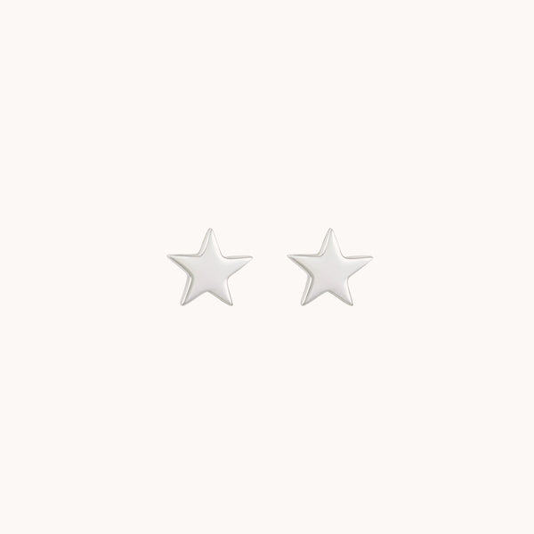 A pair of Stella earrings in sterling silver by Bluboho is displayed against a plain, light-colored background. These small, star-shaped stud earrings have a smooth, glossy finish.