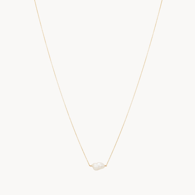 The sofia perla necklace by bluboho is a 14k yellow gold piece featuring a single irregularly shaped white pearl at its center. This minimalist and elegant design beautifully showcases the natural beauty of the pearl against the delicate gold chain.