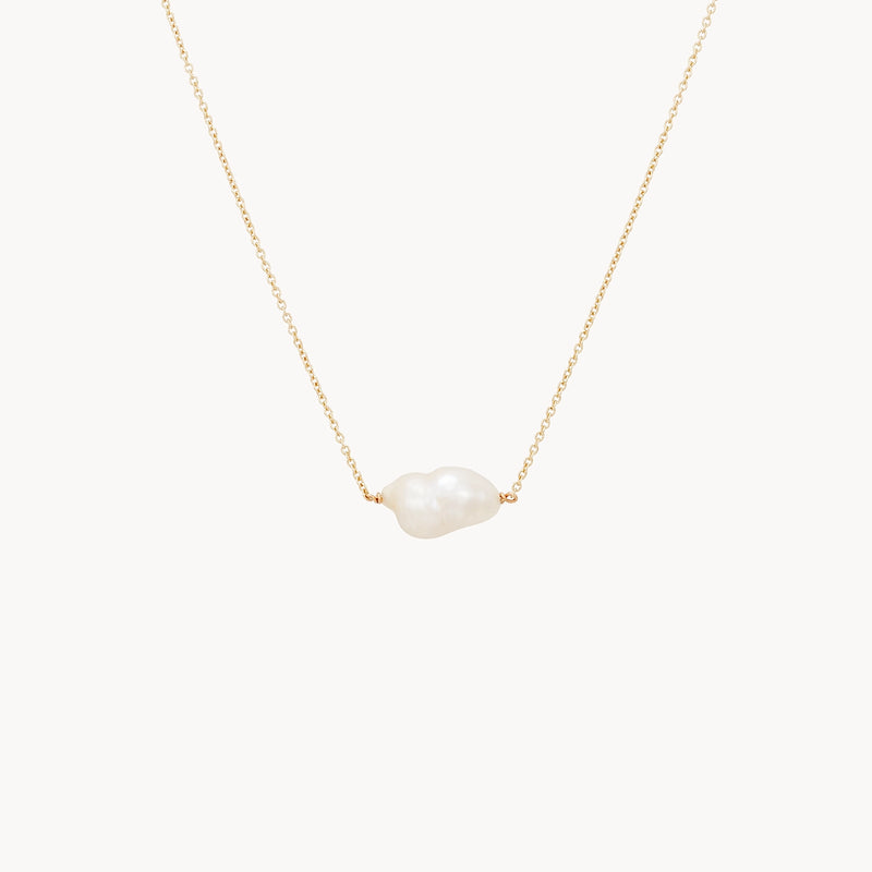 The sofia perla necklace by bluboho is a minimalist and elegant 14k yellow gold chain that showcases a single, irregularly shaped white pearl in the center. The fine, simple design of the chain ensures that the unique pearl remains the focal point.